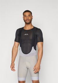 Maillot de cyclisme en mesh noir avec bretelles, accompagné d'un short rembourré gris. Le maillot porte un logo Oakley sur la poitrine.