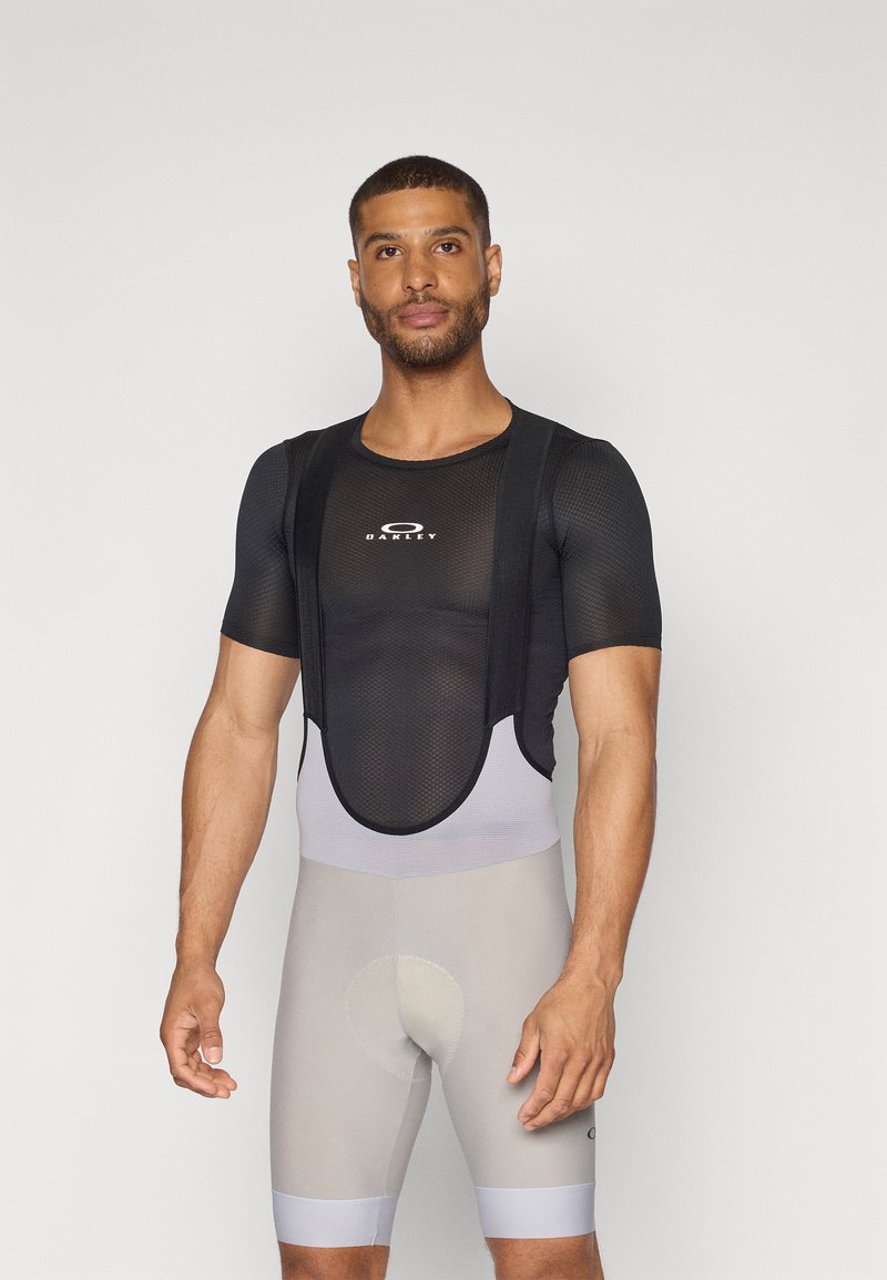 Maillot de cyclisme en mesh noir avec bretelles, accompagné d'un short rembourré gris. Le maillot porte un logo Oakley sur la poitrine.