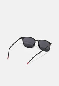 Ochelari de soare negri cu lentile întunecate, de formă rectangulară, având brațe subțiri negre cu vârfuri roșii. Material plastic neted cu o strălucire subtilă.