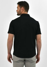 Black short-sleeve polo shirt with a classic collar, smooth texture, and a relaxed fit, shown from the back against a plain background.