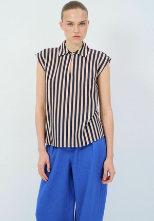 Marineblauwe en lichtbeige gestreepte mouwloze blouse met een kraag en een keyhole-detail aan de voorkant, gecombineerd met losse blauwe linnen broek.