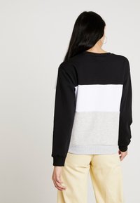 Bluza z blokami kolorów w odcieniach czerni, bieli i szarości. Wykonana z miękkiego materiału, z prążkowanymi ściągaczami na mankietach i dole. Noszona z jasnymi spodniami.