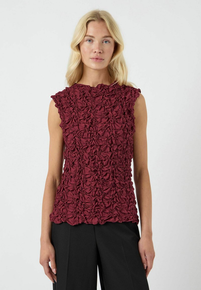 Top sin mangas burdeos con tejido texturizado y fruncido, combinado con pantalones de pierna ancha negros.
