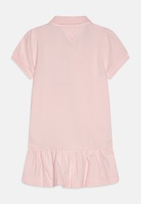 Jasnoróżowa sukienka polo z krótkim rękawem, z falbaną u dołu i prążkowanym kołnierzykiem, przedstawiona z tyłu na białym tle.