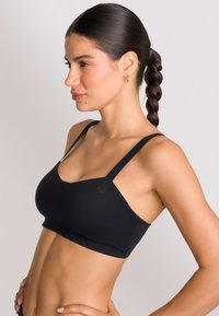 Zwarte sportbeha met dunne bandjes, een ronde halslijn en een gladde textuur. Heeft een subtiel logo aan de linkerkant.
