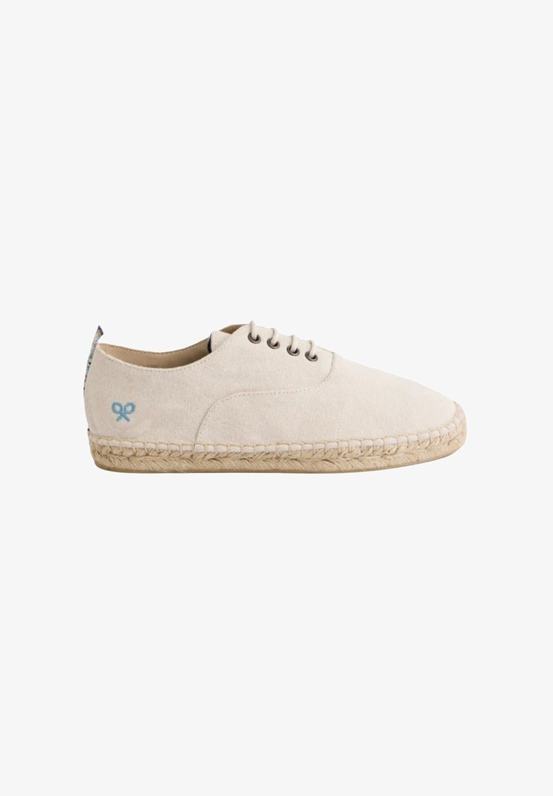 Zapato de lona beige claro con punta redondeada, suela de yute tipo espadrille, sistema de cordones con cinco ojetes y un sutil emblema azul en el costado.