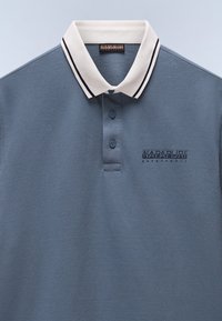 Polo in azzurro chiaro con collo a strisce bianche. Presenta una pattina con due bottoni e il logo "Napapijri Geographic" sul lato sinistro del petto.