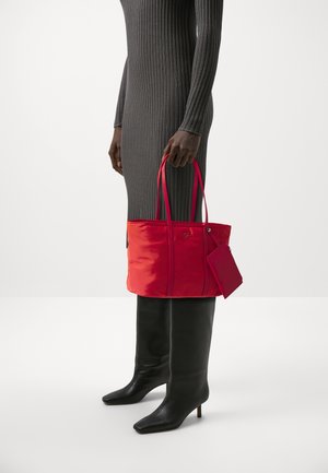 Czerwona nylonowa torba na ramię z wydłużonymi uchwytami i małą przymocowaną saszetką, charakteryzująca się gładką fakturą i minimalistycznym designem.