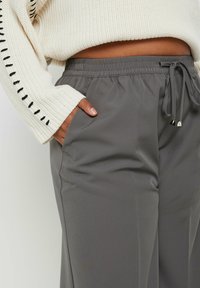 Grå byxor med elastiskt midjeband och dragsko, sidofickor och slätt, lätt tyg. Stylat med en strukturerad vit tröja.