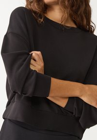 Sudadera negra con un corte relajado, mangas anchas y una textura suave. El dobladillo tiene un diseño en capas, lo que añade un detalle sutil.