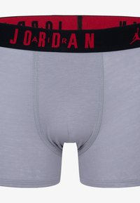 Graue Boxer-Shorts mit einem schwarz-roten Gummibund, der den Text "JORDAN" und ein Logo zeigt. Hergestellt aus weichem, elastischem Material.