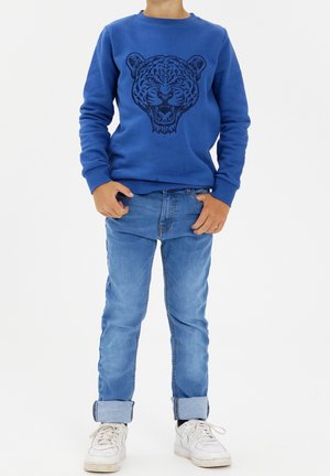 Niebieska bawełniana bluza z haftowanym wzorem tygrysa, zestawiona z jasnoniebieskimi dżinsami i białymi tenisówkami. Klasyczny krój z ściągaczami na rękawach.