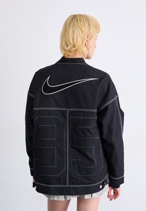 Giacca nera Nike con cuciture bianche a contrasto, vestibilità oversize, il retro presenta un logo prominente e il numero 95 in grande stampa.