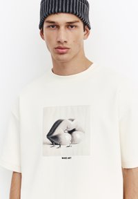 Maglietta oversize color crema con stampa grafica di labbra e testo "MAKE ART" sotto. Tessuto morbido, scollo tondo.