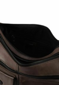 Bruine leren tas met een ritsopening, voorzien van een gestructureerd oppervlak en een zwarte binnenvoering, inclusief een extra binnenzak.