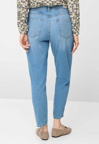 Lyseblå denim-jeans med slank pasform, der har to baglommer, en midtaljehøjde og opkrogede manchetter, kombineret med lysebrune flade sko.