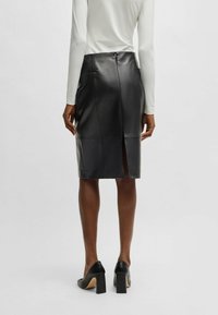 Black leather pencil skirt with a back slit, featuring smooth texture and a fitted design. The waistband has a zipper closure.