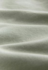 Kerge rohelise värvi puuvillane kangas, millel on sile tekstuur, mis sisaldab peeneid kortse ja voldikesi, väljendades selle kudumismustrit ja pehme tunnet.