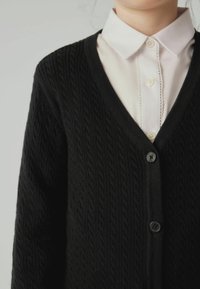 Cardigan nero con motivo a treccia testurizzato, scollo a V e bottoni frontali, indossato sopra una camicia bianca con colletto.