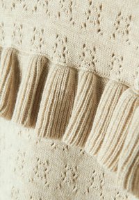 Maglione beige in maglia con un motivo testurizzato e un dettaglio a volant a coste lungo l'orlo. Materiale morbido con una consistenza leggermente ruvida.