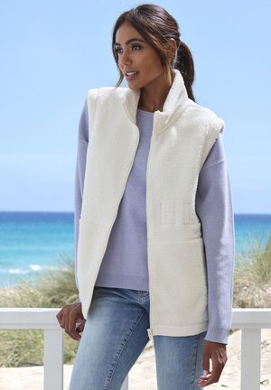 Fleece vest in cream with a high collar and zipper, featuring a textured surface, layered over a light purple sweater.
