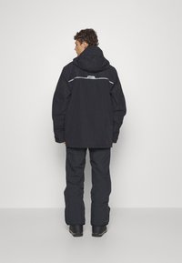 Veste noire r�ésistant aux intempéries avec capuche, bande réfléchissante et coupe ample, associée à un pantalon noir assorti et des bottes noires robustes.