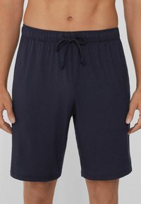 Tmavě modré sportovní šortky s elastickým pasem, stahovací šňůrkou a bočními kapsami. Hladká tkanina s uvolněným střihem a rovný cut.
