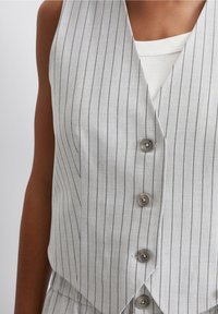 Chaleco a rayas gris con un escote en V pronunciado, con cinco botones de cierre y una textura suave, que se lleva sobre una blusa sin mangas blanca.