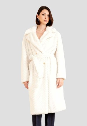 Manteau long blanc texturé avec un col châle, boutons doubles, et une ceinture à nouer à la taille. Détails en motif chevron partout.