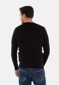 Maglione nero a collo rotondo con maniche lunghe, polsini e orlo a coste. Indossato sopra jeans in denim blu, visto da dietro. Texture liscia.