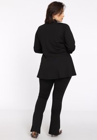 Zwart outfit bestaande uit een aansluitende top met een uitlopende zoom en bijpassende uitlopende broek. Het materiaal lijkt glad met een matte afwerking.