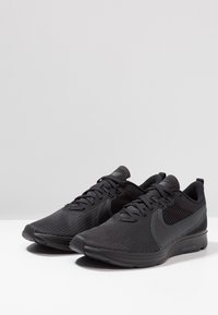 Baskets de sport en mesh noir avec un design épuré, une tige texturée, un système de laçage et un logo contrastant sur le côté. Bout rond et col rembourré.