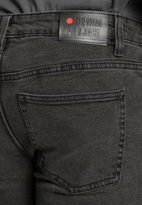Black denim jeans with a textured finish, featuring a back pocket and a leather label embossed with "DENIM PROJECT" and a red dot.