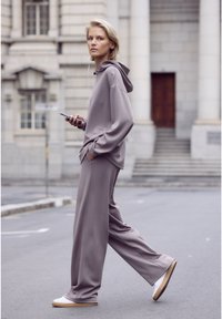 Light gray oversized hoodie and matching wide-leg pants, made from soft fabric, paired with white sneakers and a phone with earbuds.