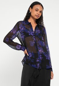 Fekete áttetsző blúz lila virágmintákkal, gombos elülső résszel és hosszú ujjakkal, gombos mandzsettákkal.