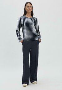 Gestreiftes, navy-blaues und weißes Langarmoberteil, kombiniert mit dunklen, weit geschnittenen Hosen. Das Outfit zeichnet sich durch ein minimalistisches Design und eine lockere Passform aus.
