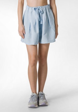 Light blue linen shorts with an elastic waistband and drawstring detail, featuring pleats for added volume. Worn with gray athletic shoes.
