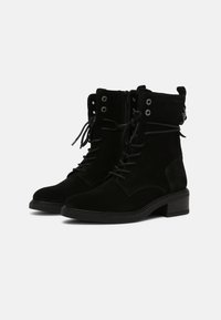 Stivali alla caviglia in suede nero con lacci frontali, occhielli in metallo e tacco quadrato piccolo. Inclusa una zip laterale per una facile vestibilità.