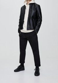 Svart läderjacka med två dragkedjefickor, vit hoodie under, svarta smalrandiga byxor och svarta sneakers med snörning.