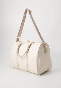 Sac de voyage beige en matériau matelassé, doté de doubles poignées supérieures, d'une bandoulière amovible et d'accents en métal doré.