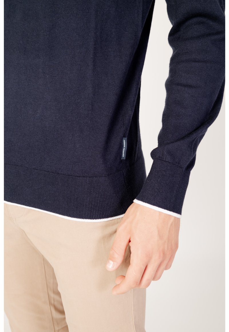 Marineblauer Strickpullover mit Rundhalsausschnitt und gerippten Bündchen, mit einem weißen Akzent am Saum. Seitliches Etikett sichtbar.