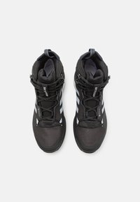 Zapatillas altas negras con material de malla y sintético, con acentos grises y suelas texturizadas, aseguradas con cordones y una tira de agarre.
