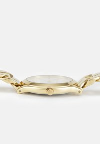 Gouden horloge met een ronde kast, een gladde bezel en een schakelsysteem. Heeft een witte wijzerplaat met gouden indexen en een kroon aan de zijkant.