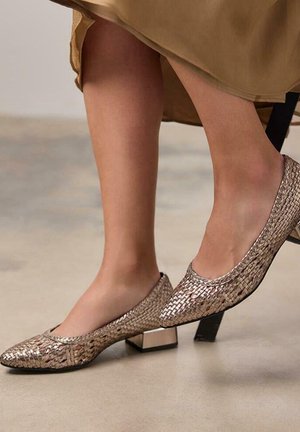Mocasines metálicos plateados con textura trenzada y tacones cuadrados, presentando un borde suave y un diseño de punta afilada.