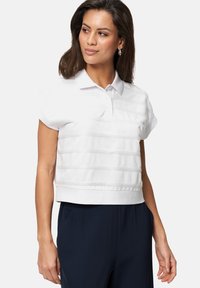 Polo blanc court à manches courtes, avec des rayures texturées horizontales et un col. Associé à un pantalon bleu marine pour le contraste.