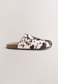 Zoccolo con stampa a mucca realizzato in materiale morbido, caratterizzato da una combinazione di colori marrone e bianco, con una resistente fibbia e cinturino. Suola piatta.