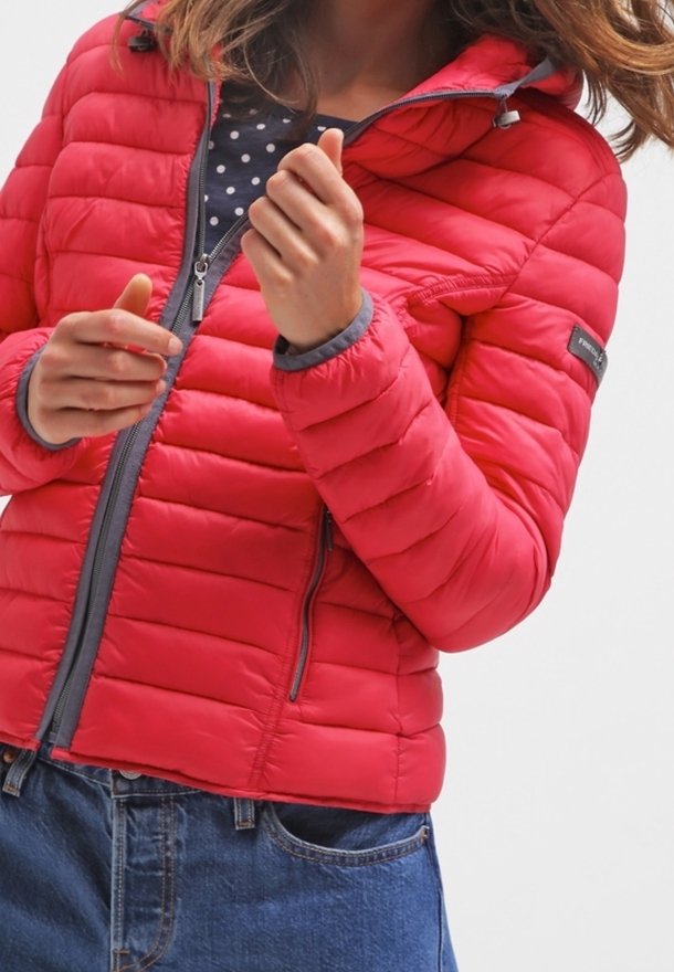 Doudoune rouge avec matelassage horizontal, fermeture éclair grise et capuche. Portée avec une chemise à pois en dessous. Coupe décontractée et manches mi-longues.