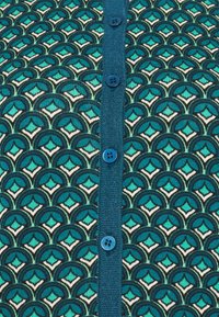 Sweter zapinany na guziki w kolorze turkusowym i czarnym, z geometrycznym wzorem, niebieskimi guzikami oraz fakturowanym, ciemnoniebieskim zapięciem.