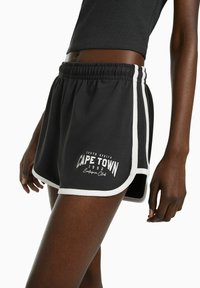 Svarta idrottsshorts med vit kant, med ett grafiskt tryck som säger "CAPE TOWN 1992" på vänster ben. Elastisk midja och avslappnad passform.