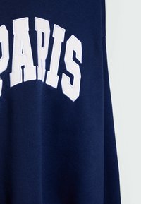 Granatowy sweatshirt z wyraźnym białym napisem "PARIS" w prostych literach. Wykonany z bawełny, o miękkiej fakturze i luźnym kroju.